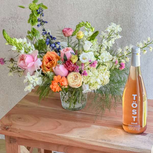 Mixed bouquet in a glass vase beside a bottle of rosé sparkling drink