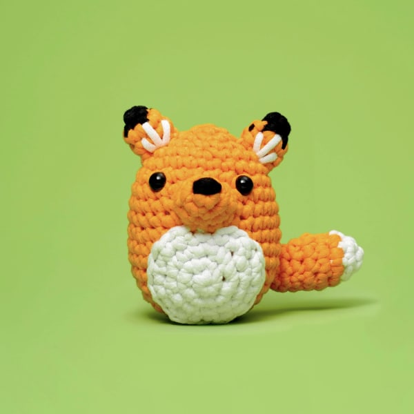 Crocheted orange fox plush with a white belly on a green background