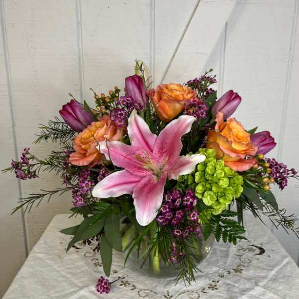 Mixed bouquet with pink lily, orange roses, and purple flowers in a glass vase