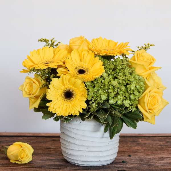 Yellow roses and gerbera daisies arranged in a white vase