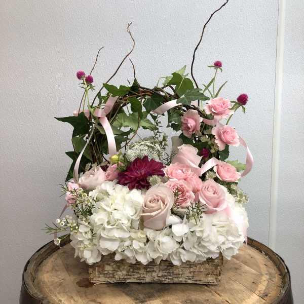 Pink and white floral arrangement in a birch bark container with ribbon