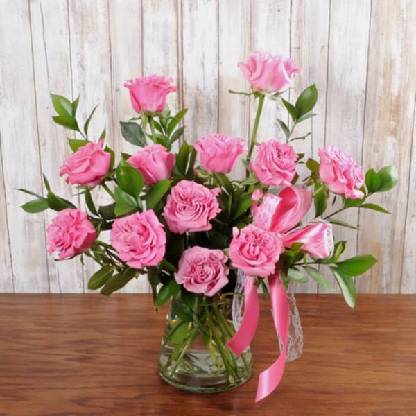 Arrangement of pink roses in a clear glass vase with a pink ribbon bow