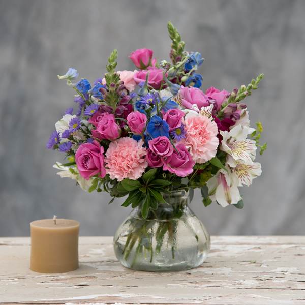 Pink and blue mixed bouquet in a glass vase beside a candle