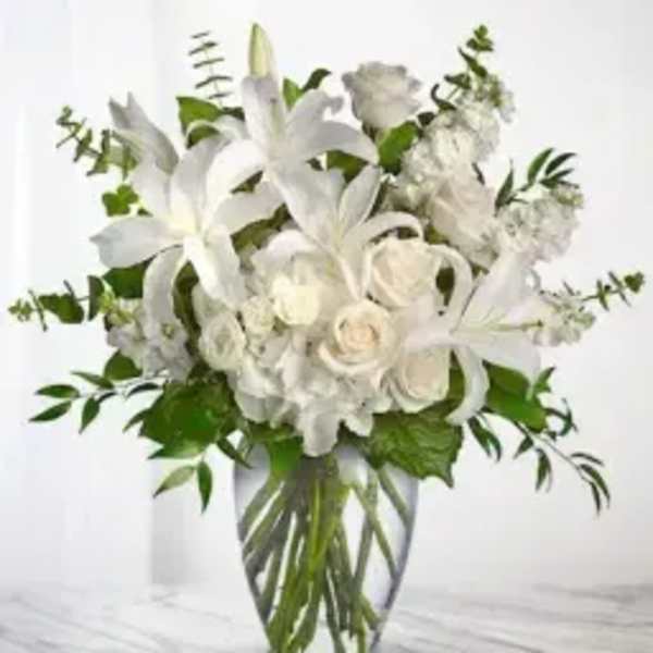 White lilies and roses arranged in a clear glass vase