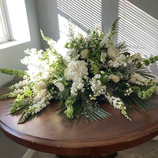 Large white floral arrangement with roses and snapdragons on a table