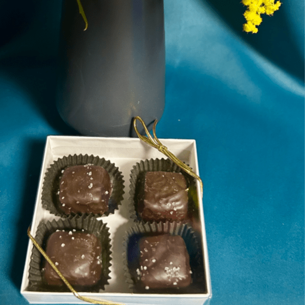 Yellow fluffy flowers in a dark vase beside a white box of four salted chocolate candies