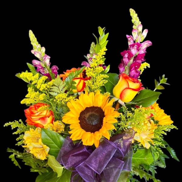 Bouquet of sunflowers, orange roses, and purple snapdragons in a glass vase