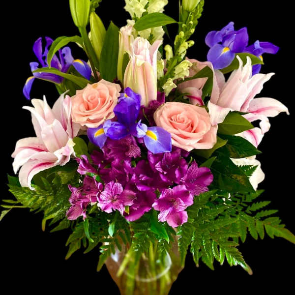 Mixed bouquet with pink roses, lilies, purple irises, and alstroemeria in a glass vase