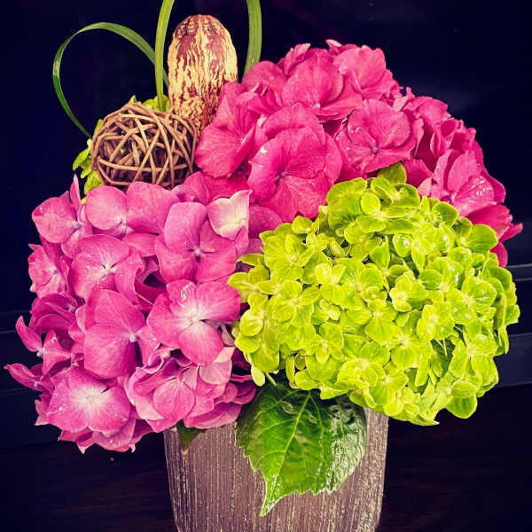 Pink and green hydrangea arrangement in a textured vase with decorative accents