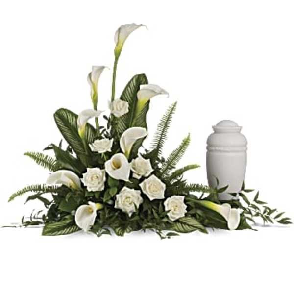 Sympathy arrangement of white calla lilies and roses beside a white cremation urn.