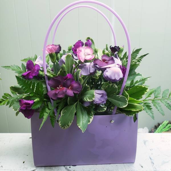 Purple and lavender flowers in a lavender handbag-style container with double handles