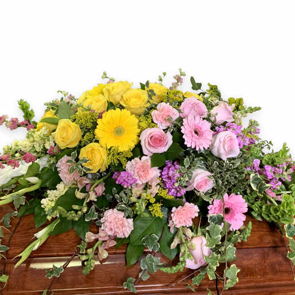 Casket spray with yellow and pink flowers and trailing greenery