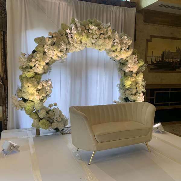 White floral arch behind a cream loveseat on a stage