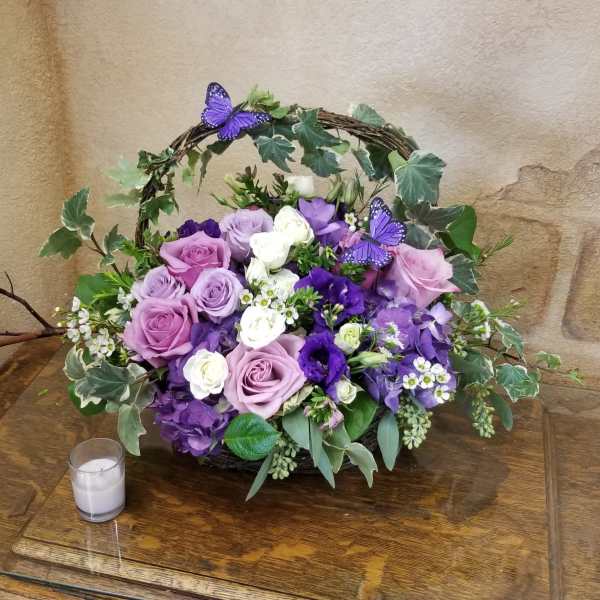 Purple and white rose arrangement in a wicker basket with ivy and butterfly accents