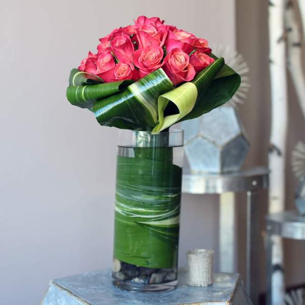 Pink roses arranged in a tall glass vase wrapped with green leaves