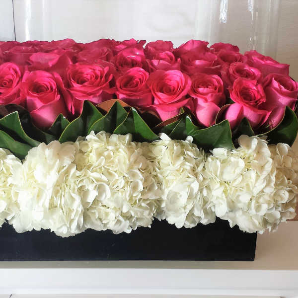 Pink roses arranged above white hydrangeas in a black rectangular box