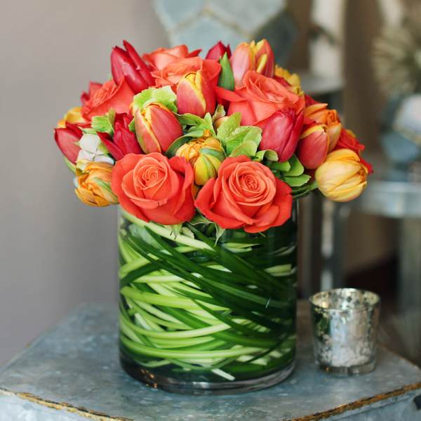 Orange roses and tulips arranged in a glass vase.