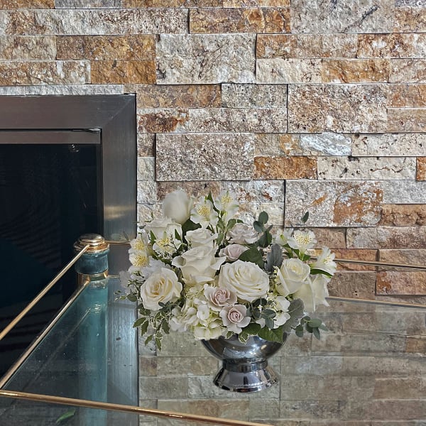 White floral arrangement in a silver urn on a glass ledge