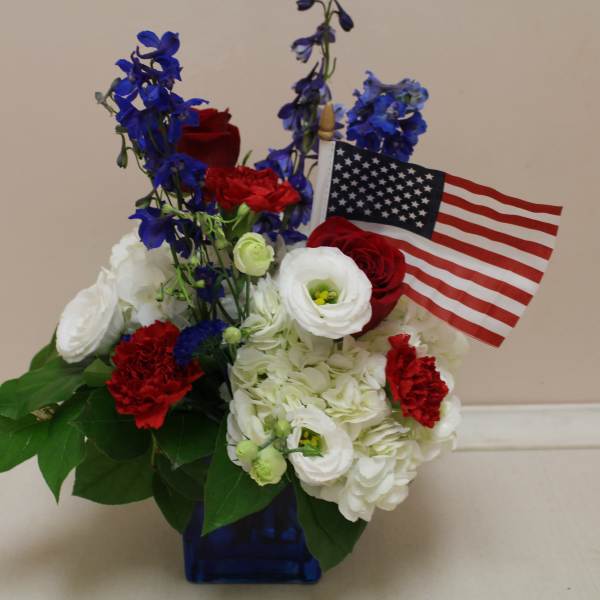 Red, white, and blue floral arrangement with an American flag in a blue vase