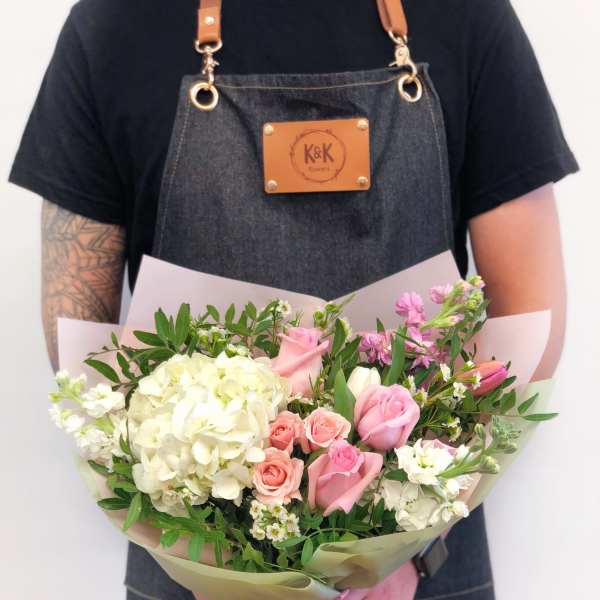 Handheld bouquet of pink and white flowers wrapped in pale paper