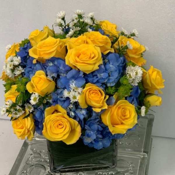 Yellow roses and blue hydrangeas in a square glass vase