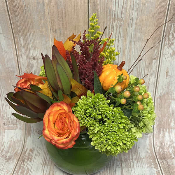 Orange rose arrangement in a green vase with pumpkins and autumn foliage