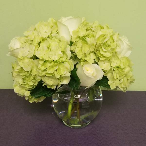 White roses and pale green hydrangeas in a clear glass vase