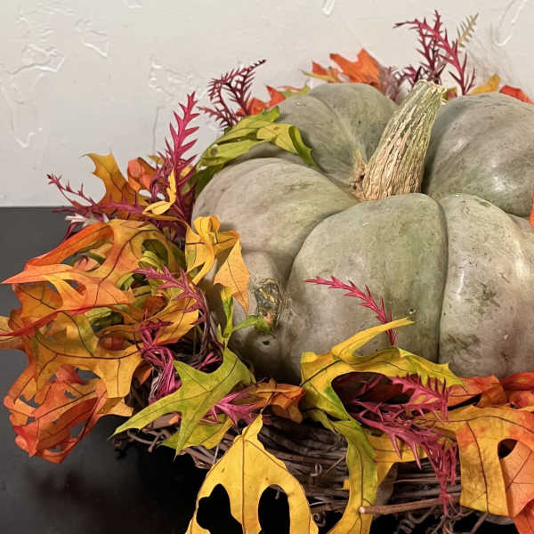 Decorative pumpkin centerpiece surrounded by autumn leaves in a wicker basket