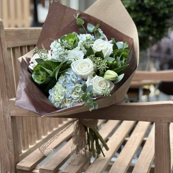 Bouquet of white roses and pale blue hydrangeas wrapped in brown paper