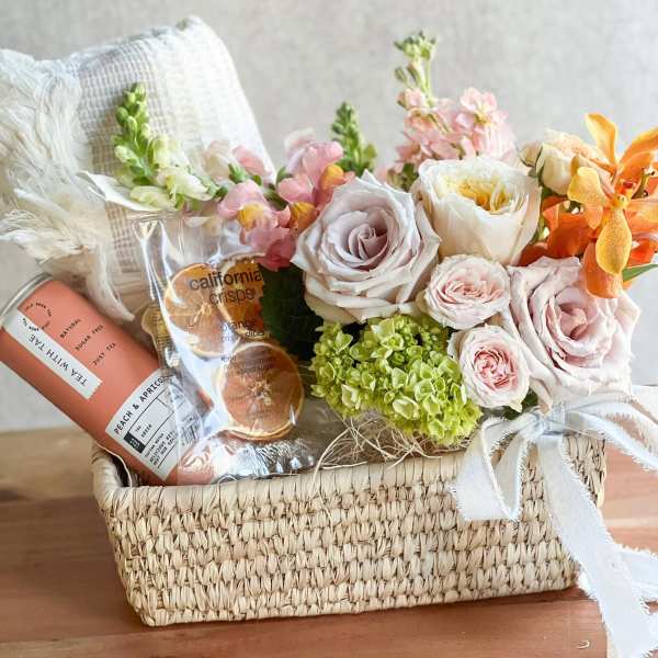 Flower and gift basket with pastel roses, hydrangeas, and snacks