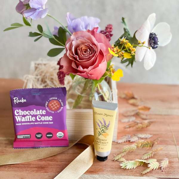 Small floral arrangement with a pink rose in a glass vase, plus chocolate and hand cream