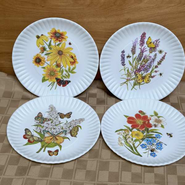 Four white plates with colorful floral and butterfly designs