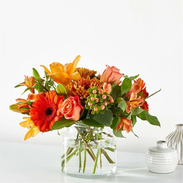 Orange and peach mixed flower arrangement in a clear glass vase