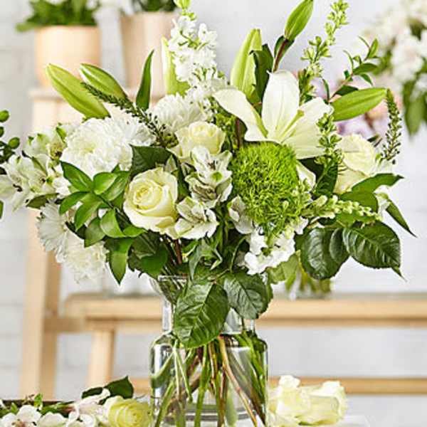 White floral arrangement in a clear glass vase with lilies and roses