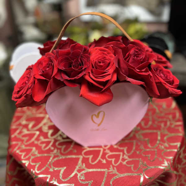 Red roses arranged in a pink heart-shaped box with a handle