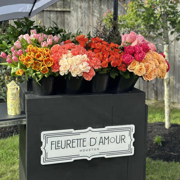 Colorful flower buckets arranged under a striped umbrella outdoors