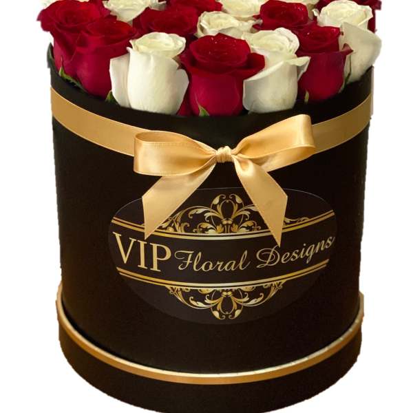 Red and white roses arranged in a black hat box with a gold ribbon