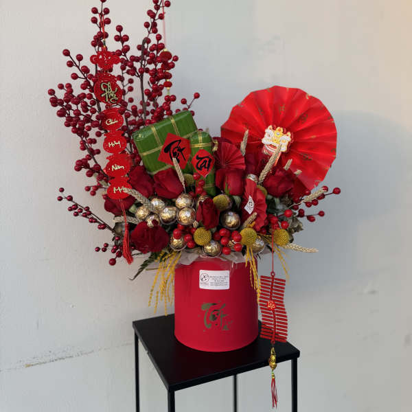 Red floral gift arrangement in a pink box with decorative fans and ornaments