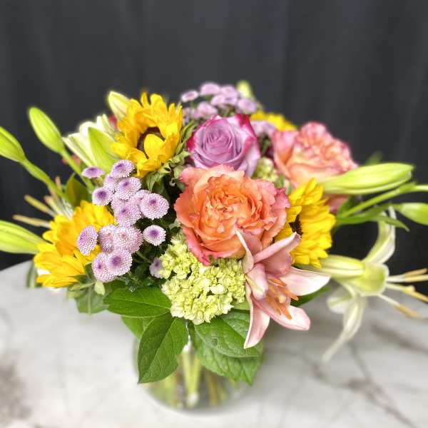 Mixed bouquet of roses, lilies, and sunflowers in a glass vase