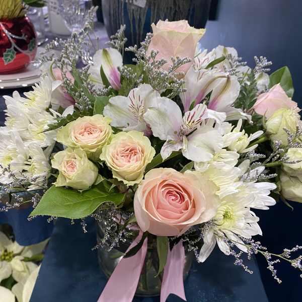Pink roses and white flowers arranged in a glass vase with a pink ribbon