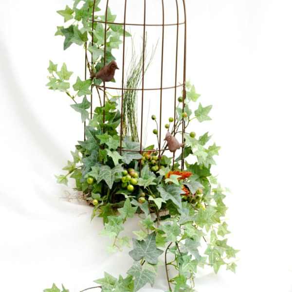 Ivy draped over a tall wire birdcage with small bird accents