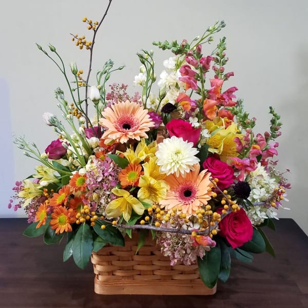 Colorful mixed flower basket with gerbera daisies, roses, snapdragons, and mums in warm tones.