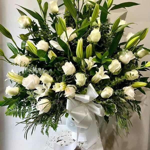 Large white lily and rose arrangement in a white vase with ribbon