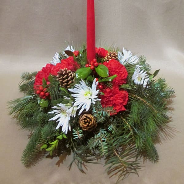 Low centerpiece of red carnations, white mums, evergreen branches and a tall red taper candle.