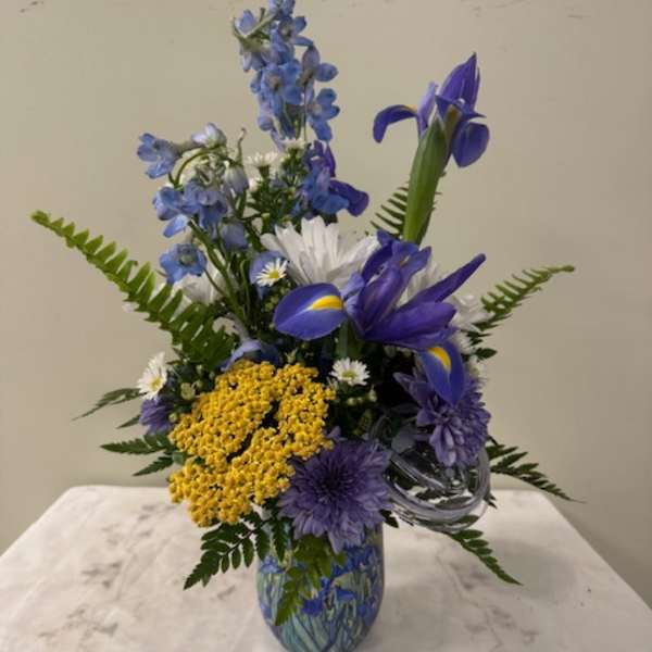Blue and yellow mixed flower arrangement in a glass vase