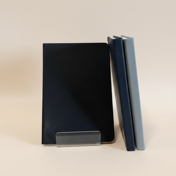 Three plain rectangular notebooks or journals in dark blue, black, and light gray