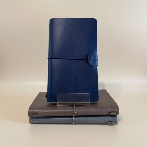 Three leather-bound notebooks stacked with a blue journal standing on top