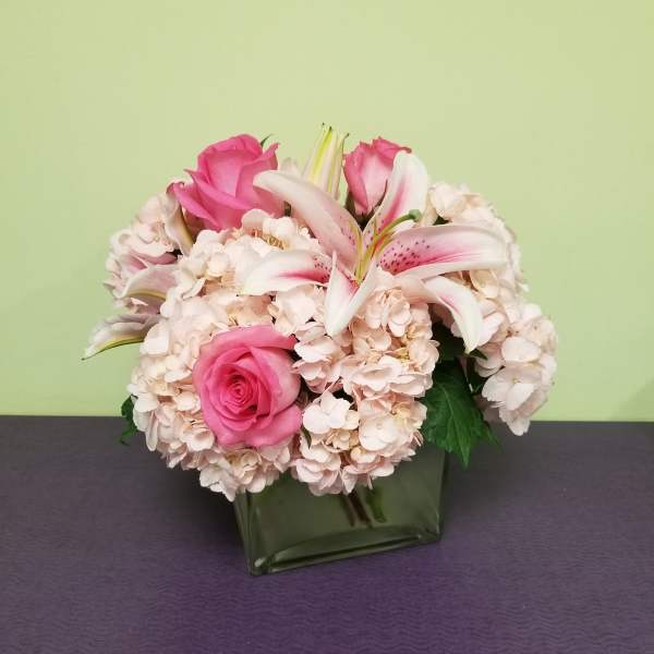Pink roses and white lilies arranged in a square glass vase