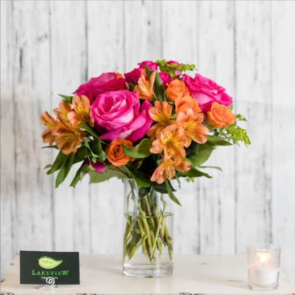 Pink and orange flower bouquet in a clear glass vase with a candle nearby