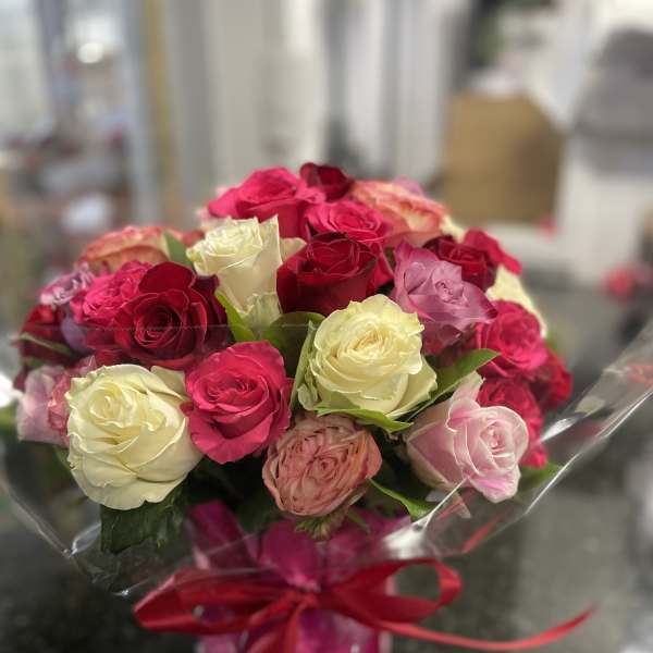 Bouquet of pink, red, and white roses wrapped in clear plastic with a red ribbon